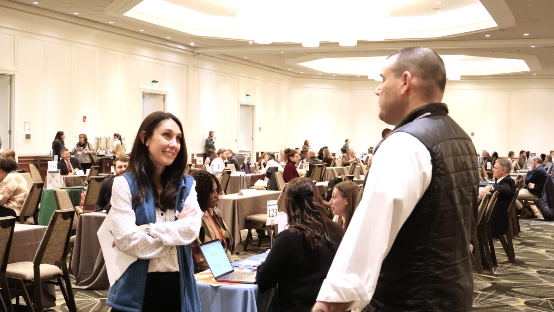 People interacting at business networking event in a conference room with tables and chairs.