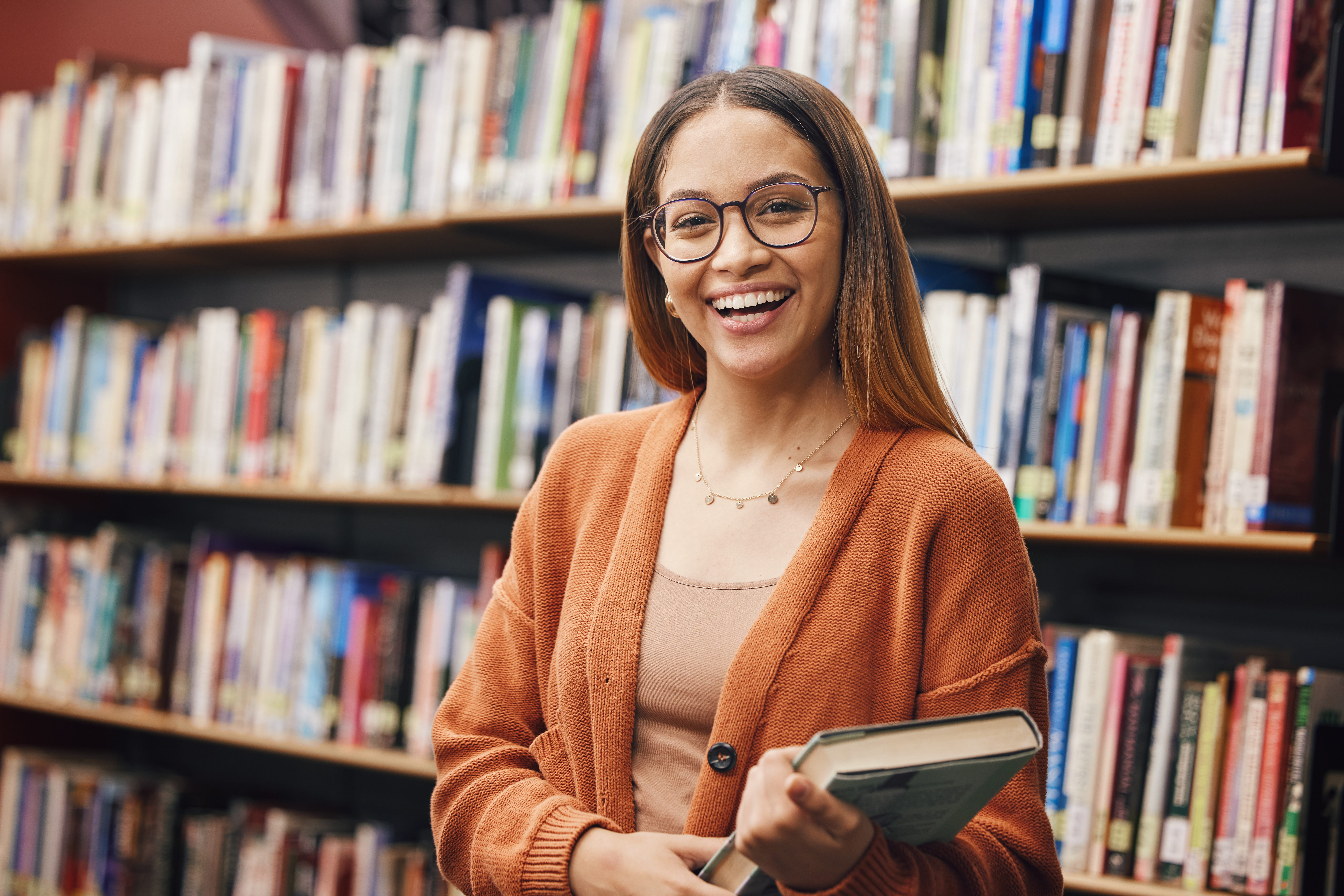 Person smiling and holding a book in a library, with bookshelves in the background.