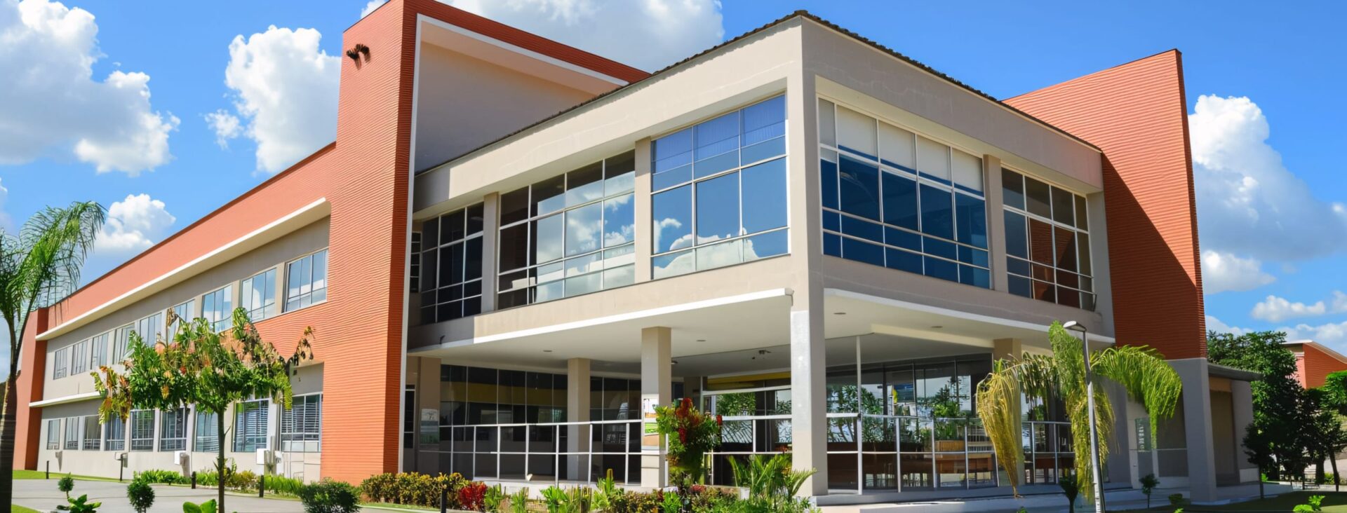 Modern two-story building with large glass windows surrounded by green landscaping and a clear blue sky.