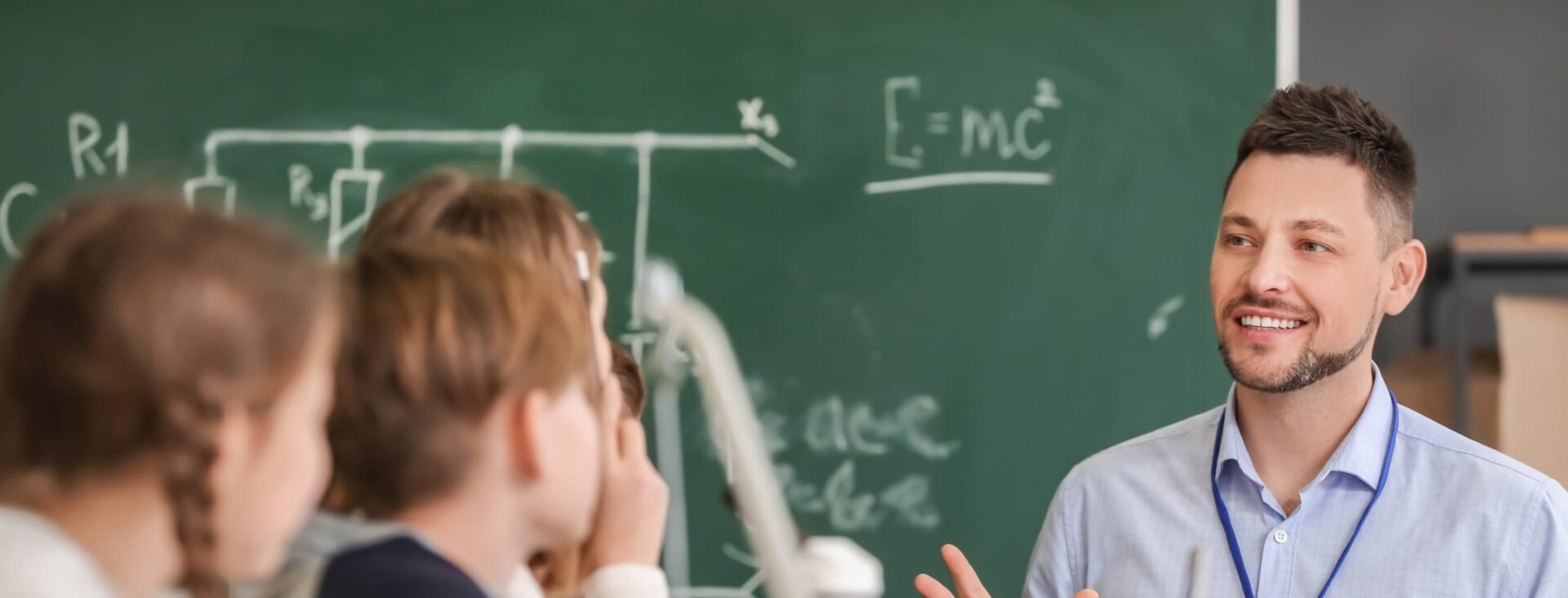 Teacher engaging students in a classroom with a chalkboard in the background.