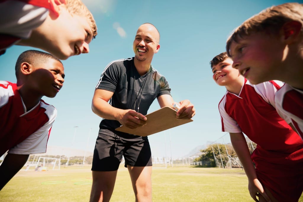 Soccer coach giving instructions to a group of young players on a sunny day at the field.