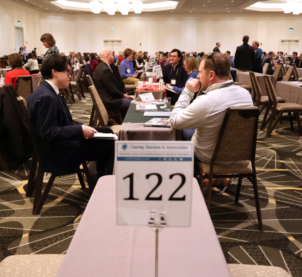 People engaged in discussions at a conference table, with a sign displaying the number 122 in the foreground.