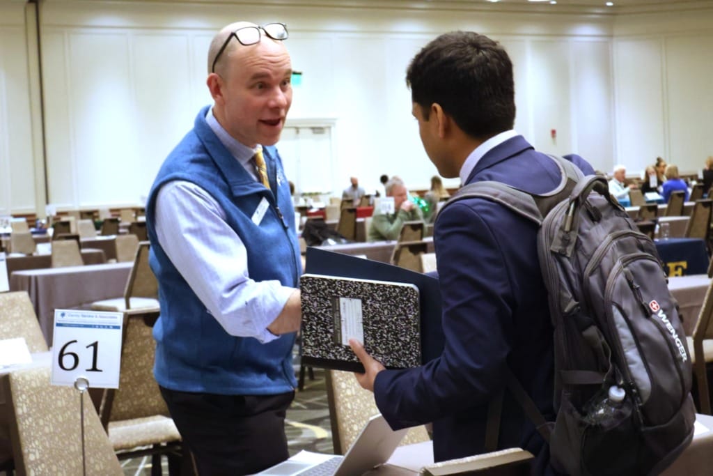 Business professional greeting a student with a handshake during a networking event in a conference room setting.