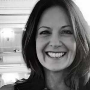 Smiling person with long hair in black and white photo, indoor setting with soft lighting.