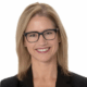 Person with glasses smiling, wearing a black blazer, against a white background.