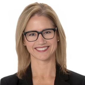 Person with glasses smiling, wearing a black blazer, against a white background.