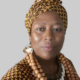 Person wearing patterned headwrap, large wooden bead necklace, and a decorative top standing against a neutral background.