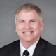 Smiling man in a suit and tie with a gray background.
