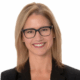 Person smiling, wearing glasses and a blazer, with a white background.