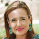 Person smiling, wearing turquoise earrings and pink lipstick, with a blurred outdoor background.