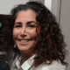 Smiling person with curly hair wearing a light-colored jacket and white shirt.