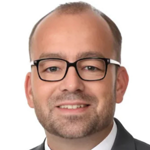 Man wearing glasses and a suit smiling at the camera.