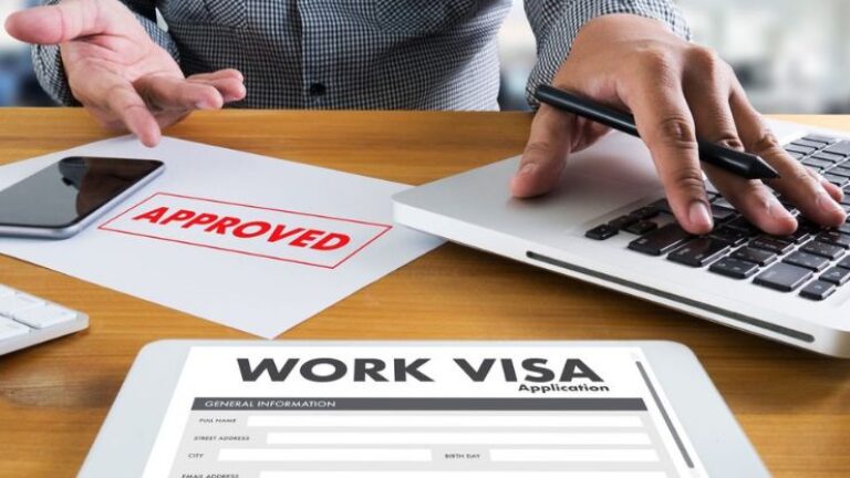 Person reviewing approved work visa application at a desk with laptop and smartphone.