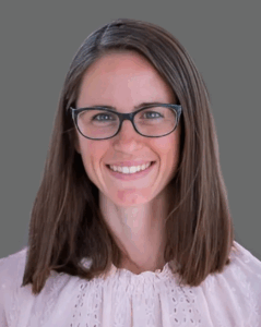 Person with glasses smiling, wearing a light pink blouse, against a gray background.
