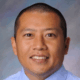 Smiling person in blue shirt against a blurred background.
