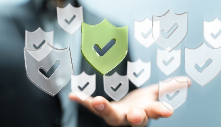 Person holding a floating green shield with checkmark, surrounded by transparent shields in a digital security concept.