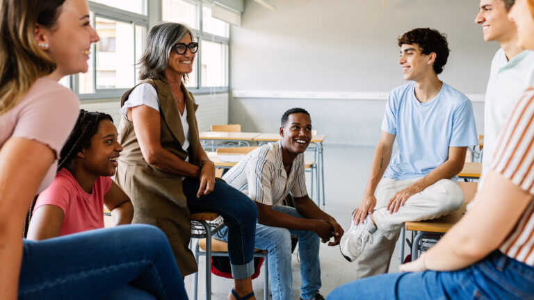 Teacher and diverse group of students sitting and talking in a classroom setting, fostering an inclusive learning environment.