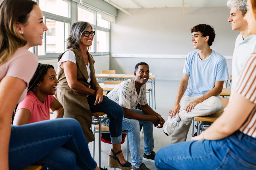 Teacher and diverse group of students sitting and talking in a classroom setting, fostering an inclusive learning environment.