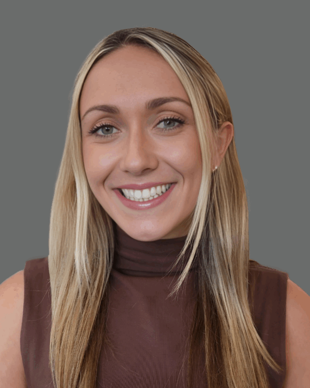 Smiling person with long blonde hair wearing a brown sleeveless top against a gray background.