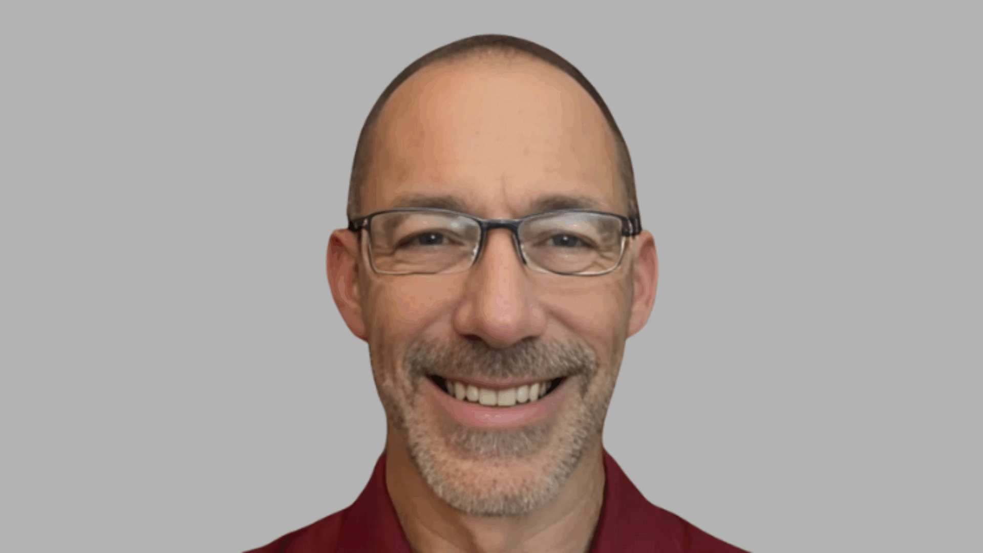 Smiling person wearing glasses and a maroon shirt against a gray background.