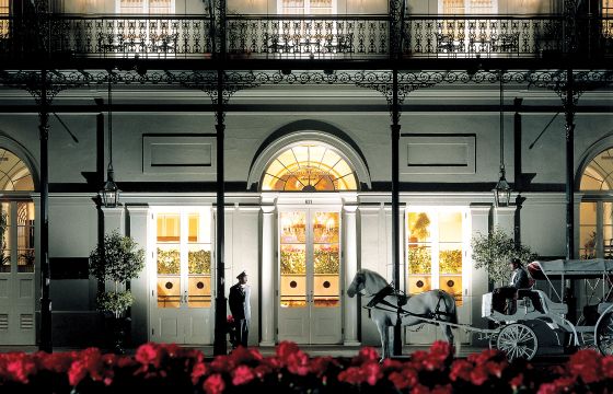 Elegant facade of a historic building with a horse-drawn carriage and lush red flowers in the foreground.