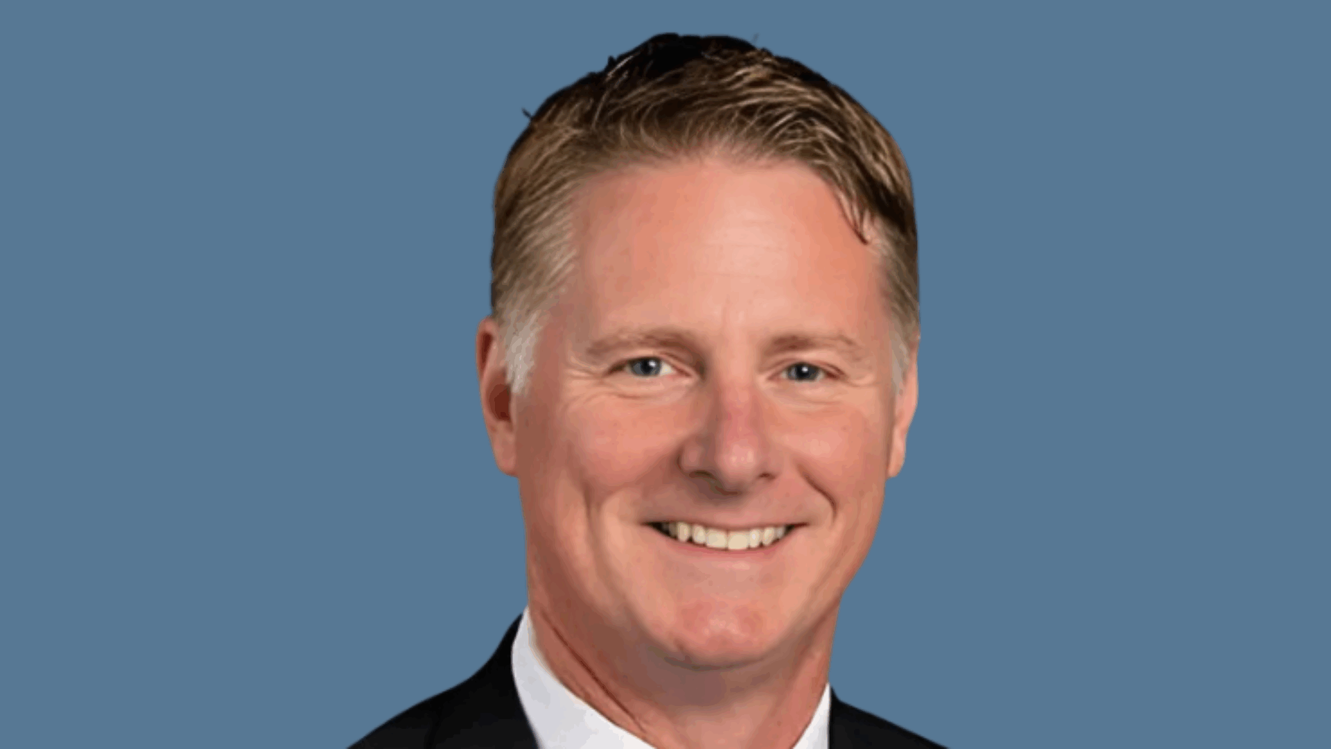 Smiling person in a suit and tie against a blue background.