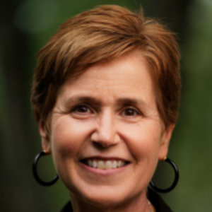 Smiling person with short brown hair and hoop earrings against a blurred green background.