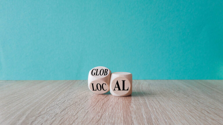 Two wooden blocks on a wooden surface against a teal background, with "GLOB LOC" and "AL" visible on the blocks.