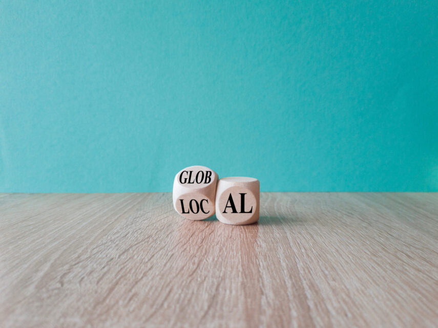 Two wooden blocks on a wooden surface against a teal background, with "GLOB LOC" and "AL" visible on the blocks.