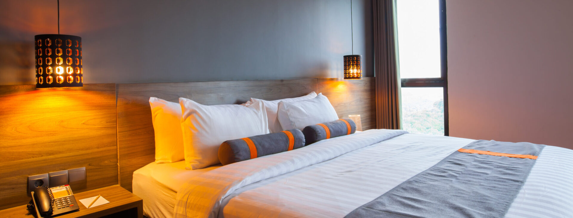 Modern hotel room with large bed, decorative pillows, warm lighting, and a window with curtains.