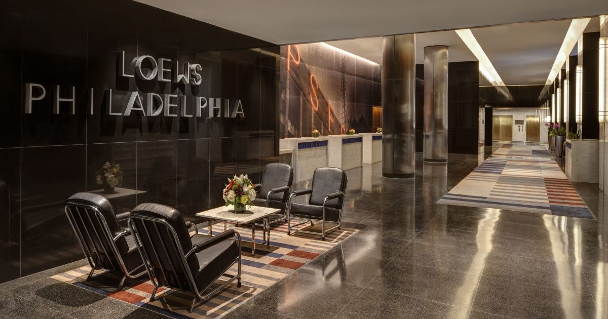 Hotel lobby with modern decor, black armchairs, small tables, floral arrangements, and checkered rugs at Loews Philadelphia.