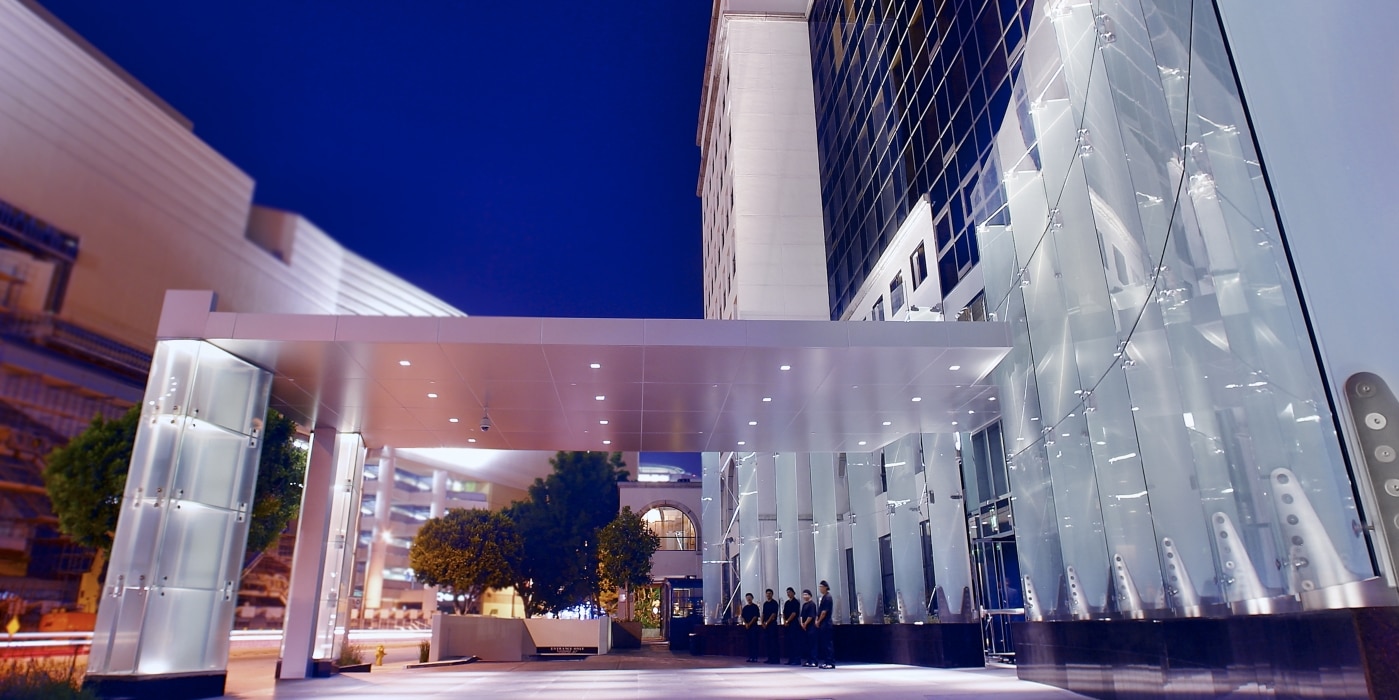 Modern office building entrance at night with glass facade and illuminated canopy, a group of people stands at the entrance.