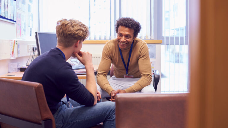 A young man in a counseling session with a therapist, sitting and talking in a well-lit office with comfortable chairs.