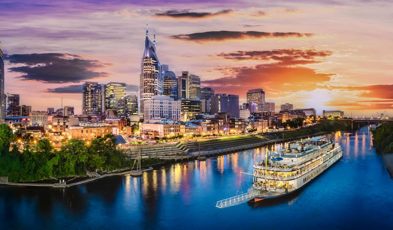 Nashville skyline at sunset with a riverboat cruising on the Cumberland River in the foreground.