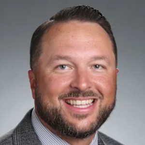 Professional man smiling in a suit and tie against a gray background.