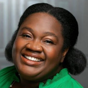 Smiling person with dark hair wearing a green top against a blurred background.