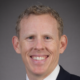 Smiling person in a suit with a grey background.