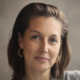 A person with brown hair and hoop earrings against a neutral background.