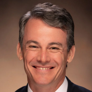 Smiling man with short gray hair wearing a suit against a plain background.