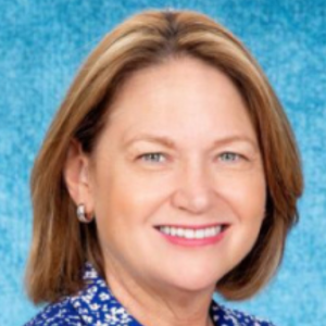 Smiling person with short hair against a blue background.